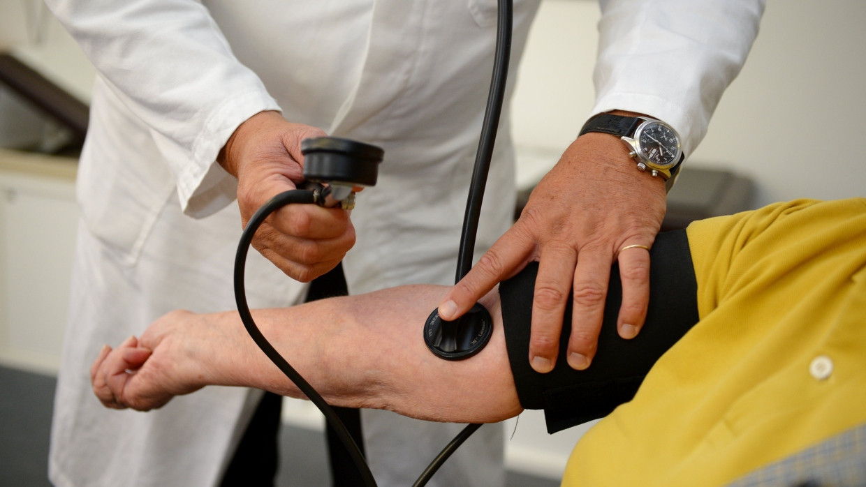 Ein Hausarzt misst bei einer Patientin den Blutdruck.