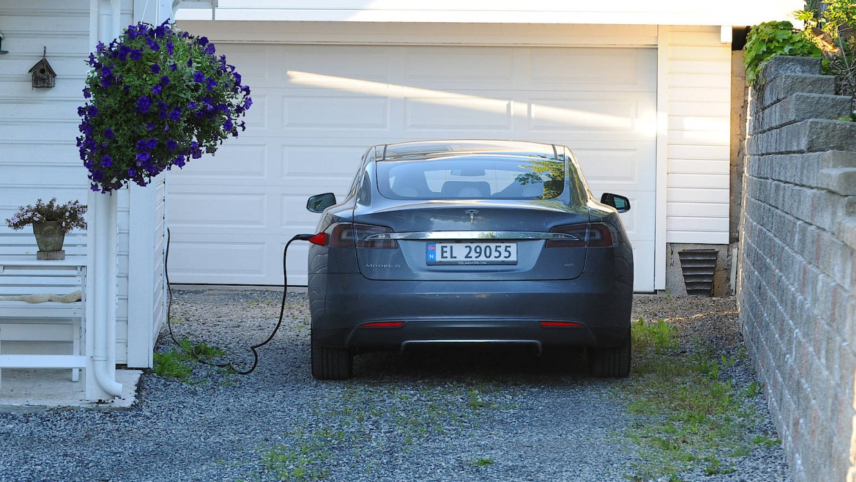 Ein E-Auto von Tesla lädt vor einer Garage in Norwegen auf.