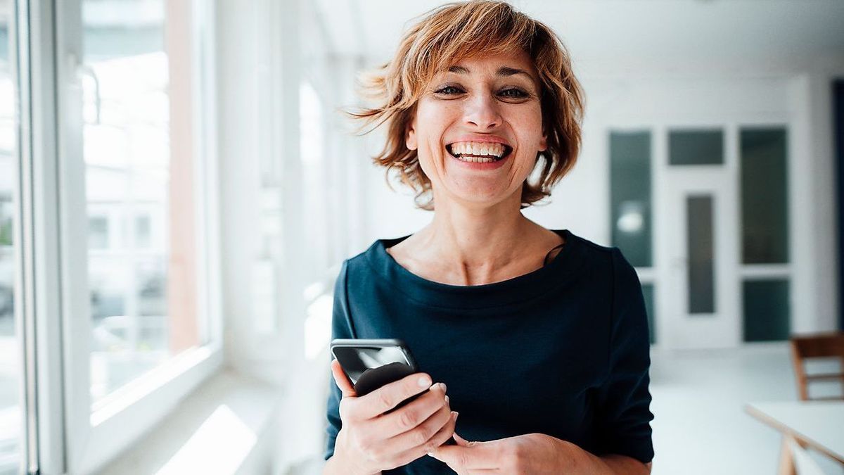 Cheerful businesswoman holding mobile phone while standing in office