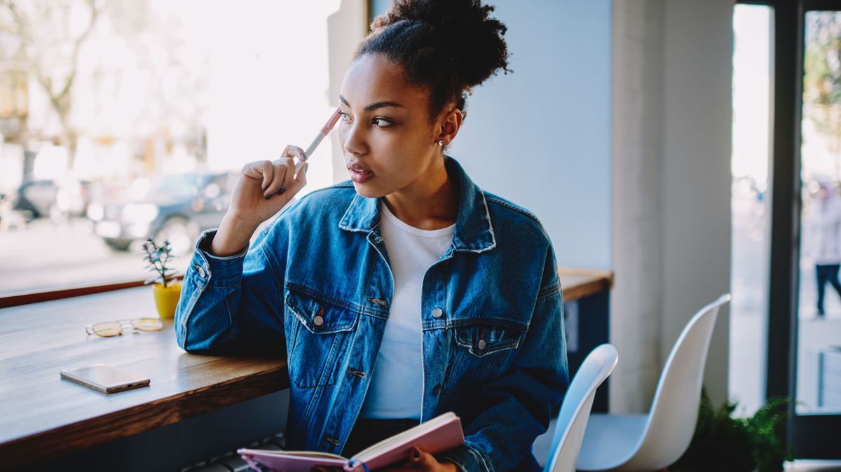Thoughtful female blogger looking away and feeling pondering on ideas for new article at own web page, pensive woman sitting in cafeteria with textbook in hand and thinking about plan for future trip
