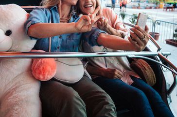 friends having fun at funfair riding roller coaster and taking selfies together