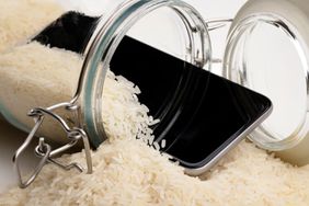 A wet smartphone is dried in rice and glass bottle on white background