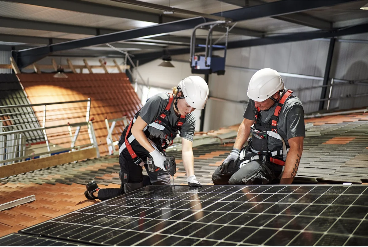 Arbeiter im blauen Monteuranzug mit weißen Helmen arbeiten an einem Panel mit Solarzellen