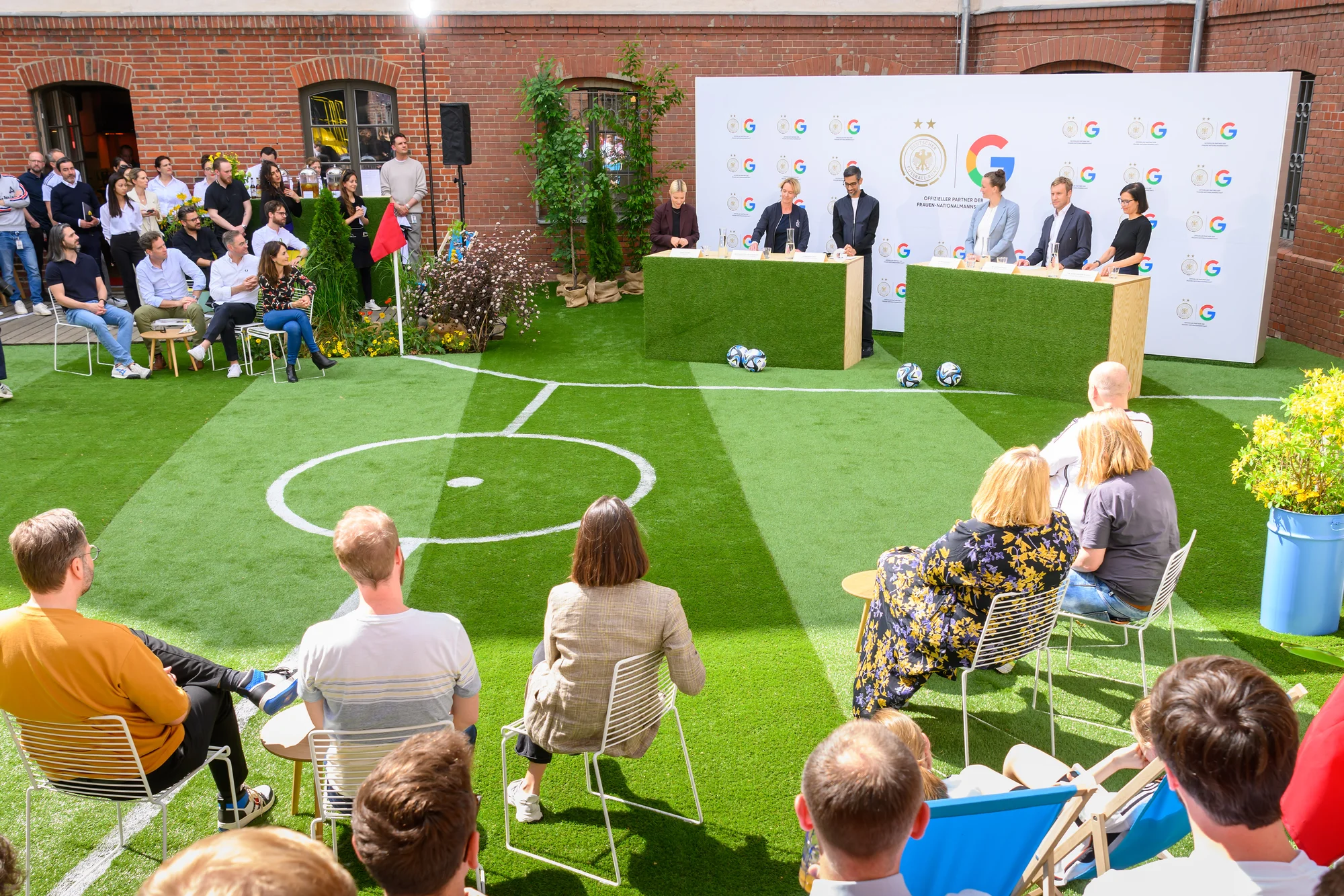 Sportmoderatorin Lena Cassel, Bundestrainerin Martina Voss-Tecklenburg, Google-CEO Sundar Pichai, Nationalspielerin Almuth Schult, DFB-Geschäftsführer Dr. Holger Blask und Dr. Anne-Katrin Huebel, Marketing-Leiterin der Google-Konsumentenprodukte (v. l.) stehen bei einer Pressekonferenz hinter grasgrünen Pulten, im Hintergrund ist eine Wand mit dem DFB- und dem Google-Logo zu sehen.